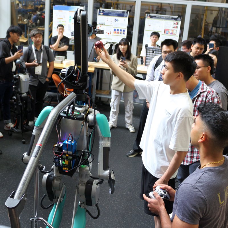 Class of students standing around a robot. One student is showing a camera on the robot an apple.